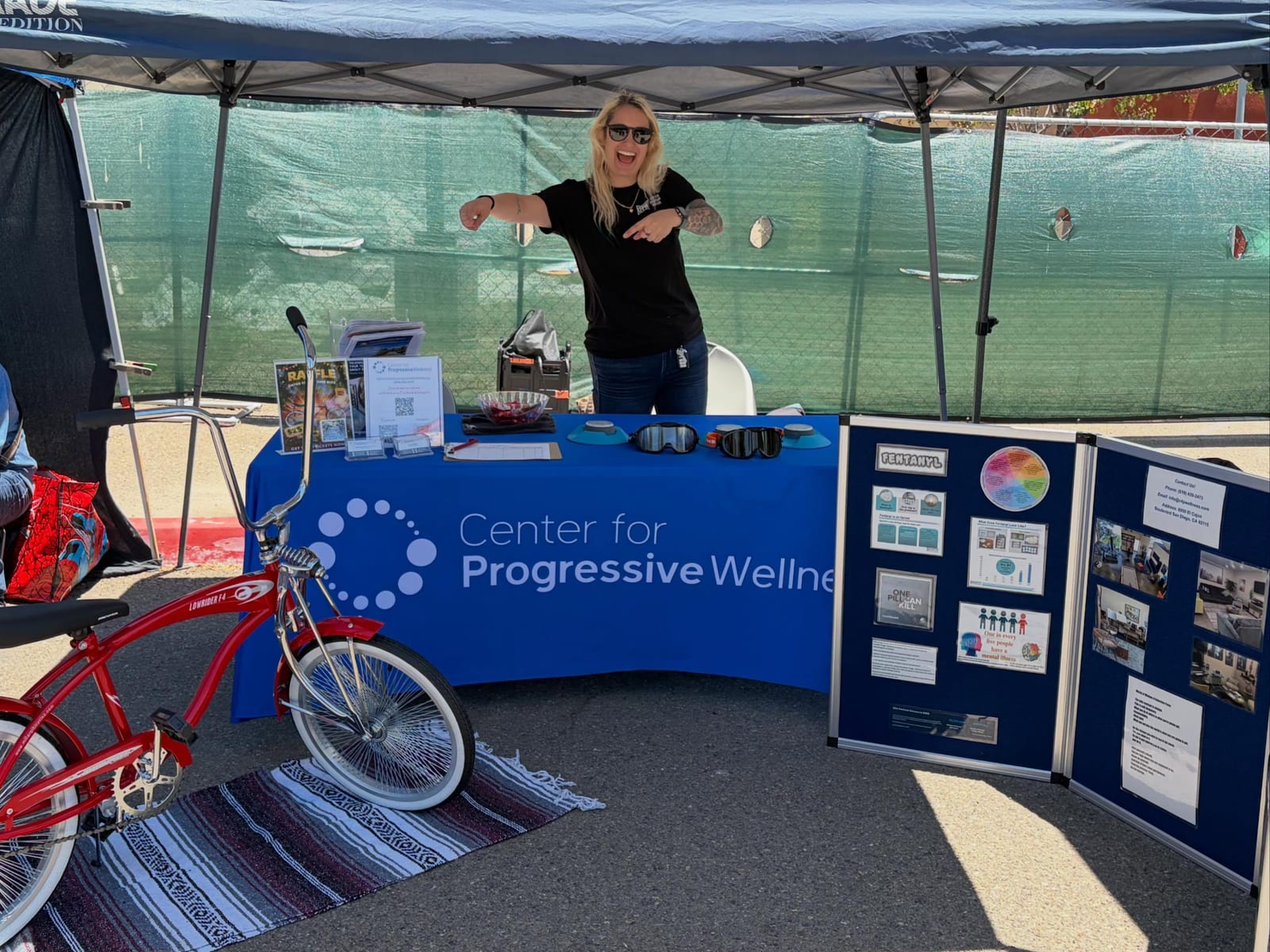 A Center for Progressive Wellness representative at a community resource booth with a red lowrider bicycle.
